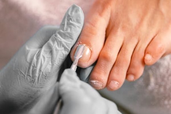 Close-up of a beautician applying nail polish on toenails during a pedicure session.